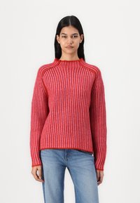 Rød og rosa stripet genser med høy hals, ribbestruktur og lange ermer. Stoffet ser mykt og koselig ut.