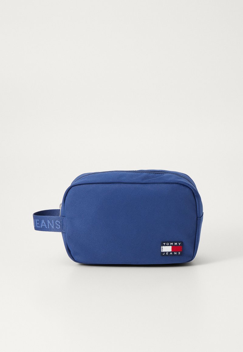 Borsa cosmetica rettangolare blu con superficie testurizzata, dotata di manico laterale e di una patch con il logo Tommy Jeans. Chiusura con zip superiore.