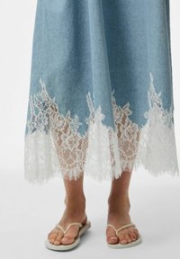 Denim svārki ar gaiši zilu tonējumu, ar baltu mežģīņu apdari ar ziedu rakstiem. Apvienoti ar baltām čībām, radot ikdienišķu izskatu.