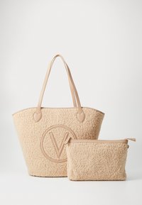 Beige texturerad tote-väska med läderhandtag och matchande zip-väska, båda med sydd cirkulär logo på framsidan, mot vit bakgrund.
