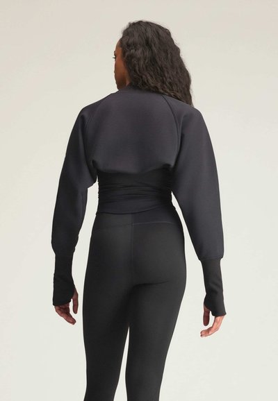 Sweat-shirt court noir avec manches bouffantes et poignets avec trou pour le pouce, associé à des leggings noirs taille haute, présentant une texture lisse.