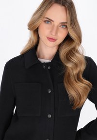 Zwarte wolmix jacket met een gekraagde halslijn, twee voorzakken en zilveren knopen; gladde textuur en getailleerde pasvorm.
