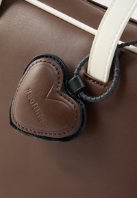 Καφέ συνθετικό τσαντάκι με απαλό υφή. Διαθέτει μαύρη και καφέ καρδιά που κρέμεται με την επιγραφή "#softlife". Λευκές τιράντες.