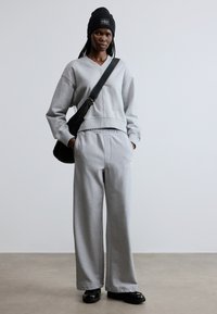 Harmaa V-kaulus collegepaita, siihen sopivat leveälahkeiset housut ja musta olkalaukku. Mallilla on musta pipo ja mustat tasapohjaiset kengät.