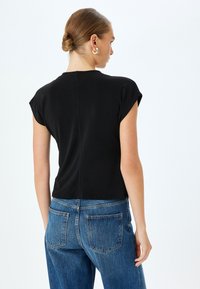 Camiseta negra corta con mangas cortas, que presenta un ligero brillo y un diseño de espalda sin costuras, combinada con jeans de mezclilla de lavado claro.