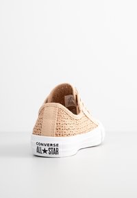 Sneaker in tela intrecciata beige chiaro con suola in gomma bianca, caratterizzata da un logo nero "Converse All Star" sul tallone e dal classico design con lacci.