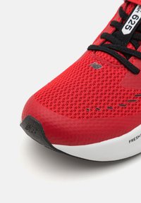 Baskets de sport rouges avec une tige en mesh respirant, des lacets noirs et une semelle intermédiaire blanche, présentant des accents de semelle extérieure noirs et des détails de logo.