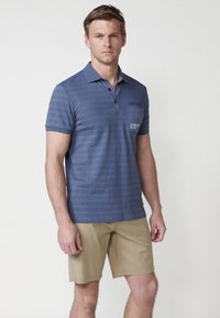 Námořnické pruhované polo tričko s klasickým límcem, tříknoflíkovou légou, krátkými rukávy a kapsou na hrudi se textem. Vše doplněno khaki šortkami.
