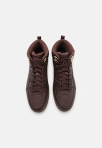 Par av bruna högskurna sneakers med guldöglor, vadderade kragar och texturerade tåkappor, visade uppifrån på en vit bakgrund.