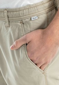 Pantalones cortos beige con una cinturilla elástica, que cuentan con un bolsillo frontal. La tela tiene una textura suave y las costuras visibles acentúan el diseño.