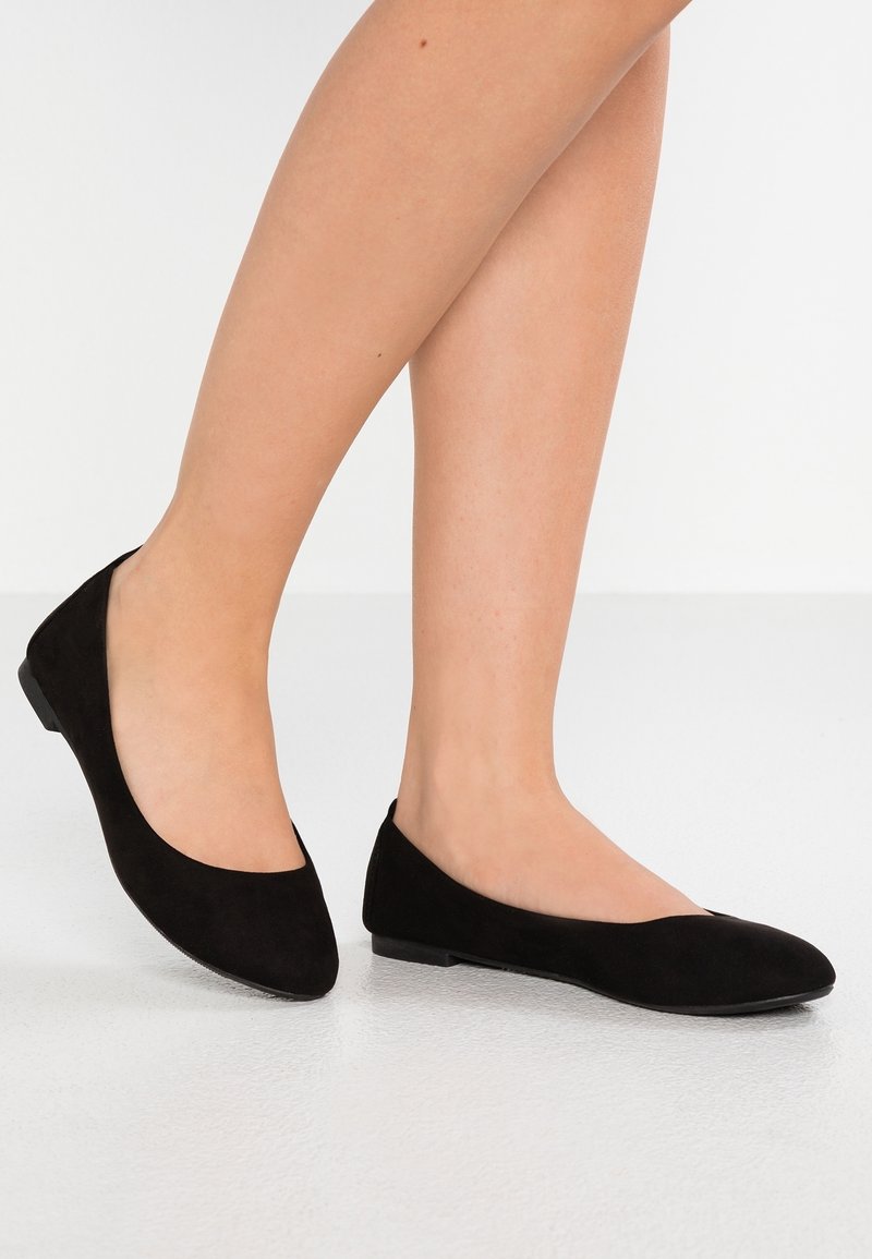 Ballerines en daim noir avec bout rond, petit talon et texture lisse. Design minimaliste sans éléments visibles ni motifs.