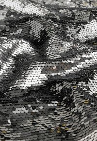 Tessuto in paillettes nere e argento con una texture liscia e una superficie riflettente, disposto in un motivo ondulato che mette in mostra dettagli scintillanti.