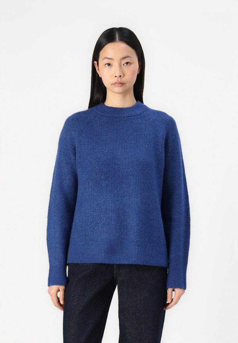 Blauwe gebreide trui met een textuurafwerking, ronde hals en geribbelde manchetten. Draag met donkerdenim broek, die een ontspannen pasvorm laat zien.