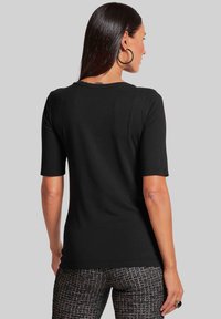 Schwarzes Kurzarmshirt mit Rundhalsausschnitt, glatter Textur, taillierter Passform und ohne sichtbare Muster, kombiniert mit gemusterten Textilhosen.