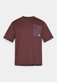 T-shirt marrone realizzato in tessuto morbido, con maniche corte e una tasca sul petto sinistro con cerniera. Include dettagli del logo sulla tasca.