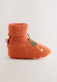 Chausson bébé tricoté orange avec bord-côtes, feuille verte brodée et petits points décoratifs blancs et bleus sur le côté.