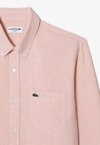 Camicia button-up di colore rosa chiaro con tessuto texture, vestibilità regular e logo di coccodrillo ricamato sul taschino del petto.