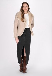 Veste en fausse fourrure beige avec grands revers, associée à une jupe en denim noire à fente avant et des bottes à talons marron.