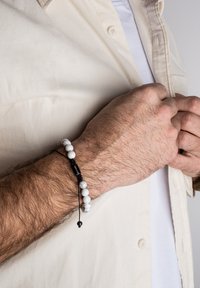 Pulsera con cuentas de mármol blanco y cordón ajustable negro. El diseño presenta un cierre simple con una cuenta de acento negra.