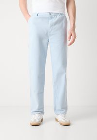 Lyseblå bomullsbukser med rett ben-design, utstyrt med sidelommer og synlig knappestolpe. Sammen med hvite joggesko.
