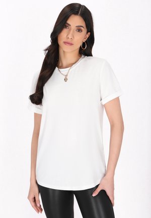 Hvid kortærmet T-shirt med rund halsudskæring og opkrøllede ærmer. Glat, letvægtsstof med en buet kant, kombineret med sorte leggings.