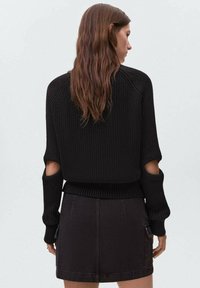 Črna pletena jopica z izrezanimi detajli na rokavih, z ribasto teksturo in prilegajočim dnom. V kombinaciji z črno denim krilom.