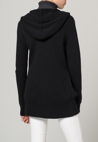 Czarna dzianinowa bluza z kapturem o teksturowanej powierzchni, z ribbowanym dołem i odpinanym szarym wewnętrznym kołnierzem, widziana z tyłu.
