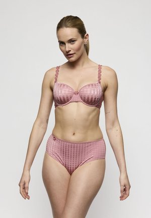 Vrouw model met bijpassende roze textuur beha en hoge taille slip, staand tegen een effen lichtgrijze achtergrond.