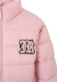 Veste matelassée rose clair avec un col haut, fermeture éclair à l'avant, et un écusson bordé de noir portant des lettres "JR" texturées sur la poitrine.