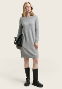 Robe en tricot grise à manches longues et décolleté rond, associée à des bottes en caoutchouc noires montantes et un sac à main noir.