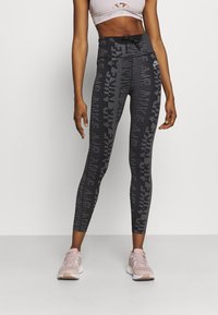 Svartmönstrade leggings med hög midja som har texten "NIKE AIR". Modellen bär en ljusrosa crop-top och matchande sneakers.