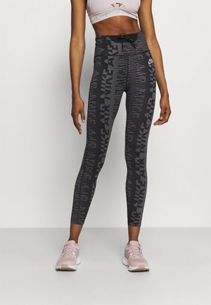 Leggings negras con estampado y cintura alta que presentan el texto "NIKE AIR". El modelo lleva una camiseta corta de color rosa claro y zapatillas a juego.