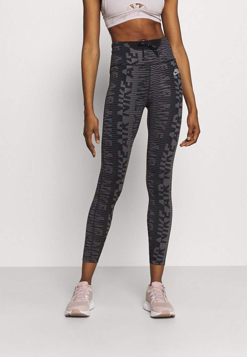 Svartmönstrade leggings med hög midja som har texten "NIKE AIR". Modellen bär en ljusrosa crop-top och matchande sneakers.