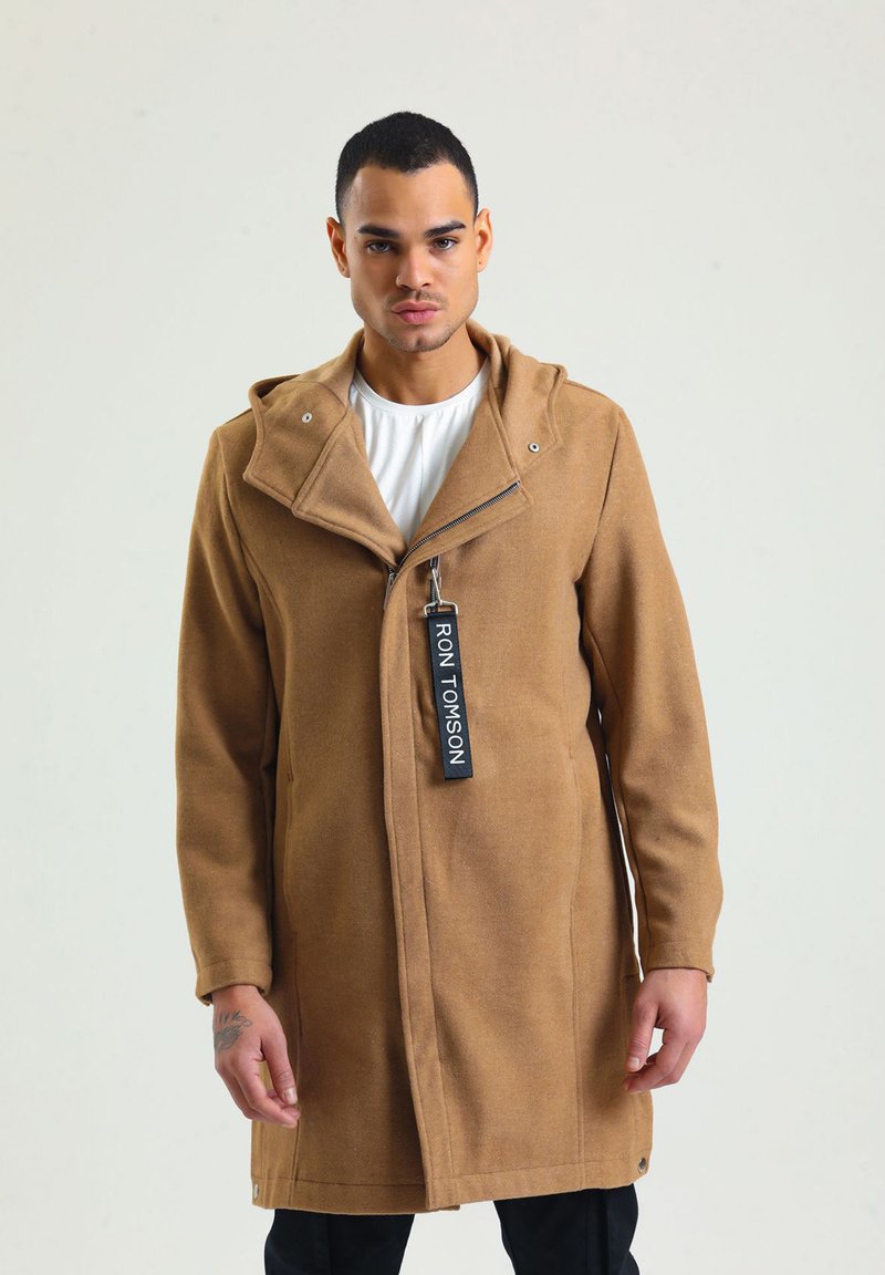 Beige Wollmantel mit Kapuze, ausgestattet mit einem Reißverschluss, einem ausgeprägten Kragen und einem Etikett mit der Aufschrift "RON TOMSON." Das Design hat eine gerade Schnittführung.