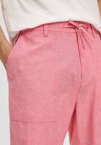 Lichtroze linnen broek met een trekkoord in de taille, zijzakken en subtiele textuur, getoond vanaf de taille naar beneden.