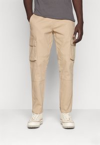 Pantalones cargo beige hechos de una tela ligera, con múltiples bolsillos laterales, un corte recto y secciones de rodilla reforzadas.