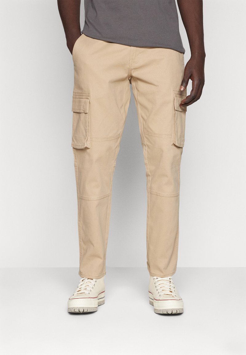 Pantalones cargo beige hechos de una tela ligera, con múltiples bolsillos laterales, un corte recto y secciones de rodilla reforzadas.