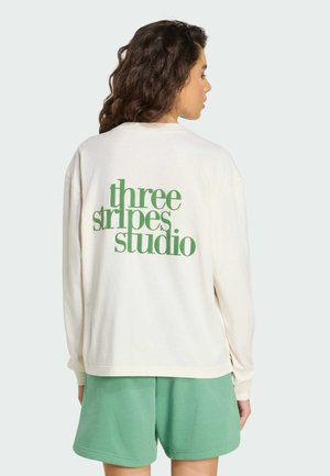 Sweat-shirt couleur crème avec texte vert "three stripes studio" au dos, associé à un short vert menthe. Tissu doux, coupe décontractée, manches longues.