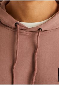 Sudadera de algodón rosa con un bolsillo canguro en la parte frontal, cordones negros y un pequeño logo negro en la zona del pecho.