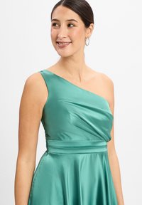 Smaragdgroene satijnen jurk met een schouderontwerp, gedrapeerde lijfje en aansluitende taille. Gladde textuur met een vloeiende rok.