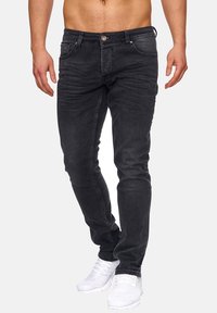 Musta farkut slim fit -leikkauksella, joissa on etutaskut, näkyvät ompeleet ja nappisuljenta, yhdistettynä valkoisiin urheilukenkiin.