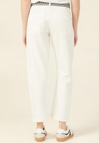 Jeans bianchi a gamba larga con orli arrotolati e una cintura a motivo; abbinati a sneakers bianche con dettagli neri.