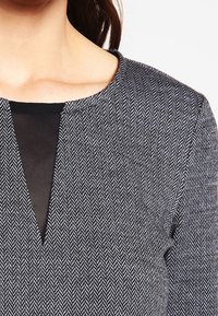 Czarna i biała bluzka w wzór houndstooth z okrągłym dekoltem i siateczkowym wstawieniem na środku, wykonana z gładkiego, teksturowanego materiału.