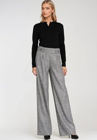 Czarna bluzka z długim rękawem zestawiona z szerokimi szarymi spodniami w wzór, które mają wysoki stan, duże guziki i gładką teksturę. Całość dopełniają czarne szpilki.