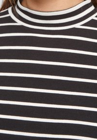 Musta-valkoinen raidallinen pystykauluksellinen paita, joka on valmistettu pehmeästä puuvillasekoitteesta. Paidan ominaisuuksiin kuuluu tasaiset vaakaraidat ja istuva malli.