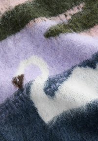 Strickdecke in einer Mischung aus Pastellfarben, darunter Flieder, Grün und Blau, mit einem Muster eines Schwans vor einem strukturierten Hintergrund.