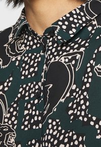 Overhemd met knopen, voorzien van een zwarte achtergrond met groene en crèmekleurige abstracte patronen, korte kraag en donkere knopen voor sluiting.