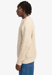 Kabelgebreide trui in off-white met een textuurafwerking, geribde manchetten en een casual pasvorm, gecombineerd met blauwe denim jeans.