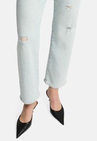 Scarpe slingback nere in pelle con punta affusolata, abbinate a jeans in denim azzurro chiaro strappati con orlo sfilacciato e strappi sulle ginocchia.
