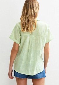 Grönrandig kortärmad skjorta i lättviktigt tyg, med en bak söm och en avslappnad passform. Bärs med denimshorts.